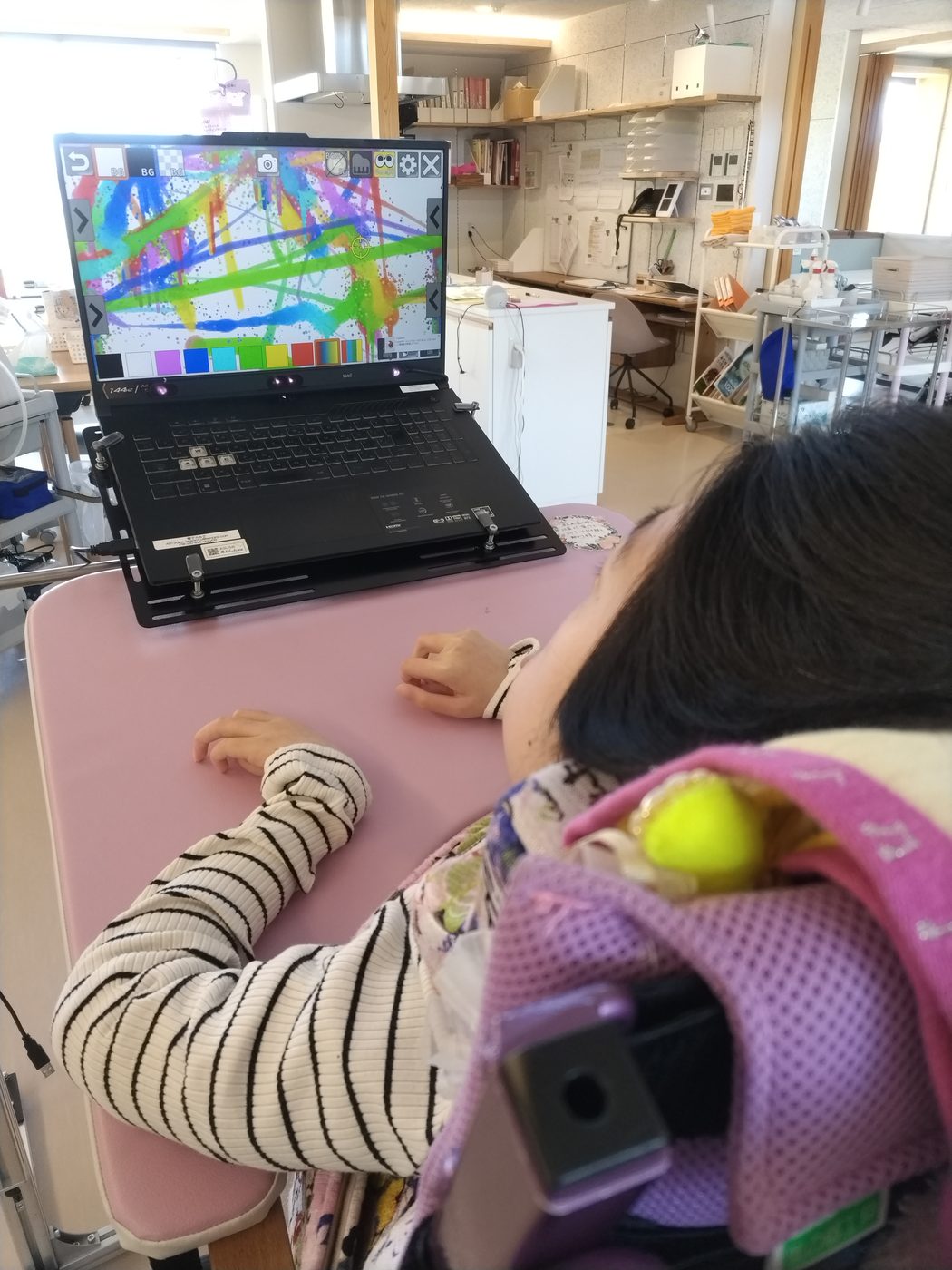車いすの学習者がパソコンの画面を見つめ、画面には色とりどりの線が描かれている